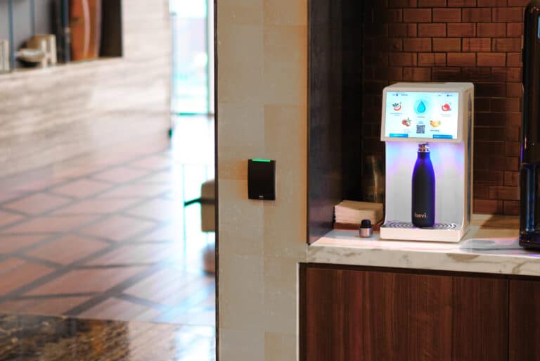 Bevi countertop water dispenser in office kitchen with a man and woman holding beverages and talking to each other