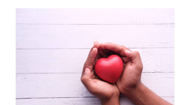 Two hands cupping a heart-shaped red fruit