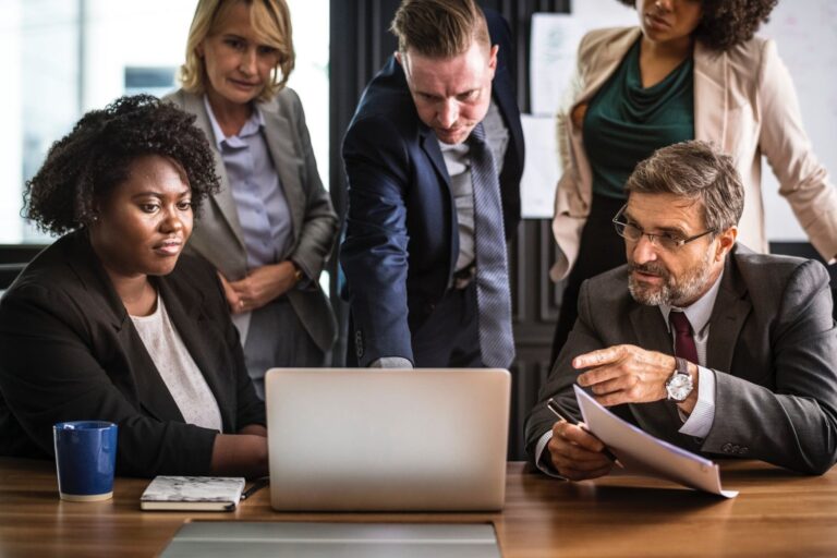 Four office workers gathered around a laptop computer