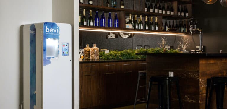 the standup bevi water dispenser next to a bar with a shelf displaying wine bottles