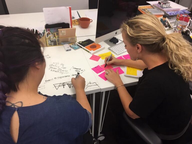 Two women working side by side at a large office table