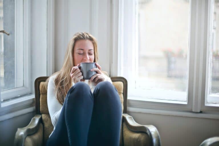 woman sitting in a chair with her knees to her chest, drinking a cup of coffee