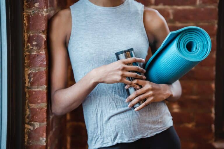 Woman holding a reusable water bottle and yoga mat