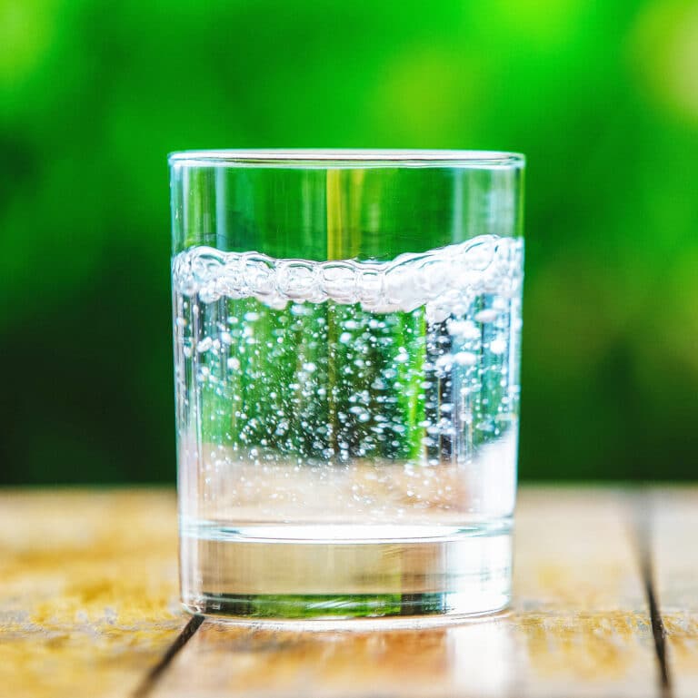 rocks glass filled with sparkling water on table with green background