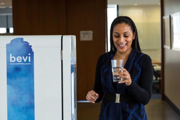 Smiling woman holding a glass of water next to a Bevi standup machine