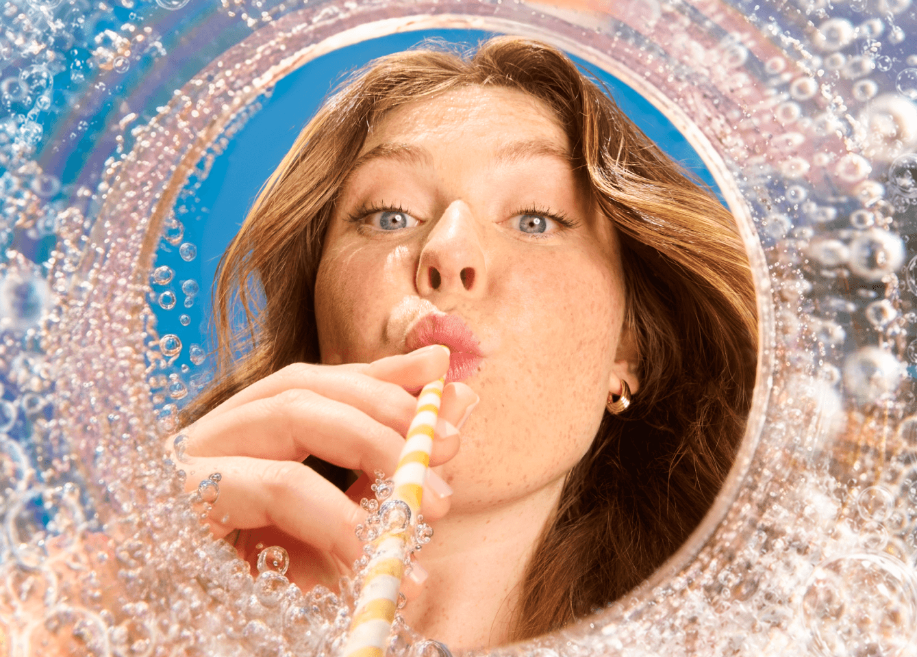 Woman sipping BeviPop through a straw, seen through a fizzy glass