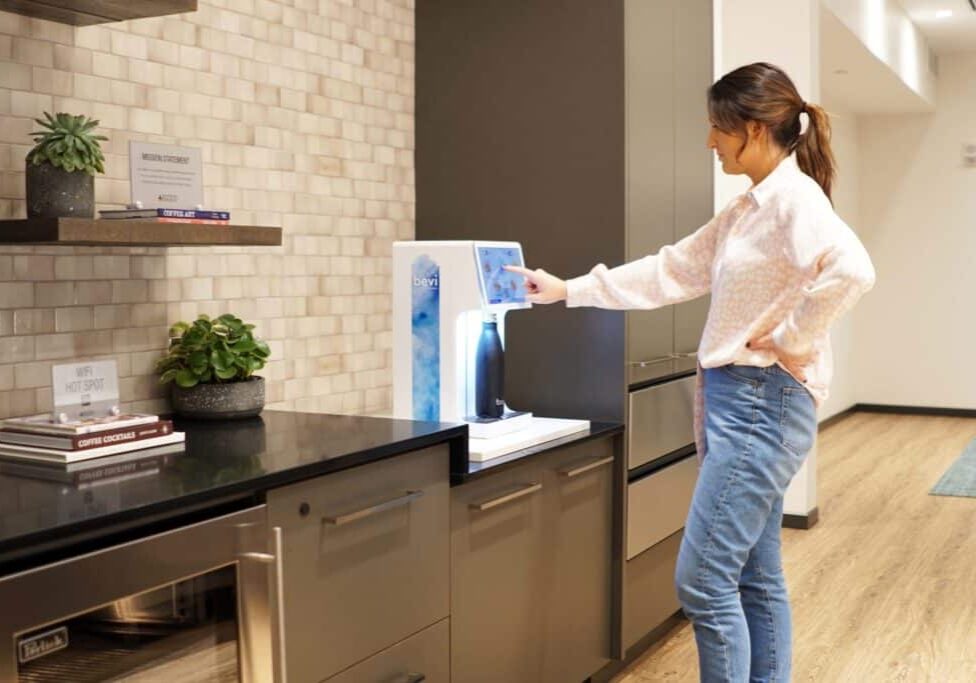 Woman using the Bevi Countertop machine in an apartment amenity lounge