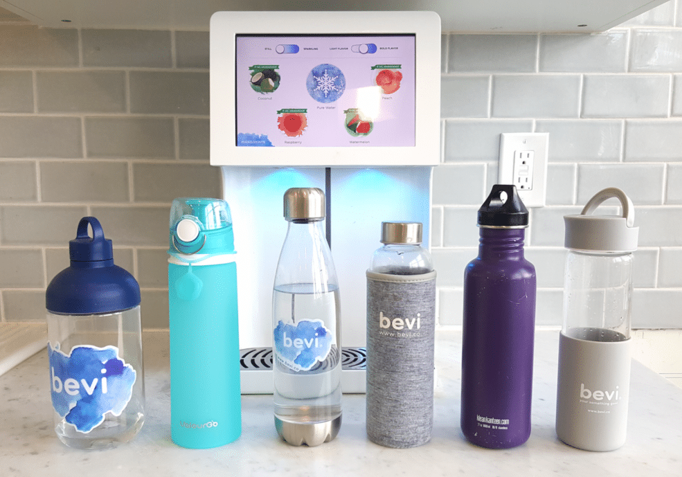 Several reusable water bottles on a counter in front of a Bevi Countertop machine
