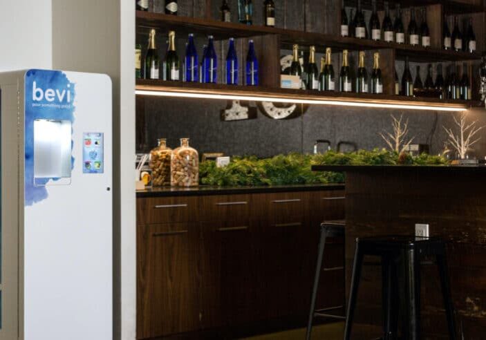 the standup bevi water dispenser next to a bar with a shelf displaying wine bottles