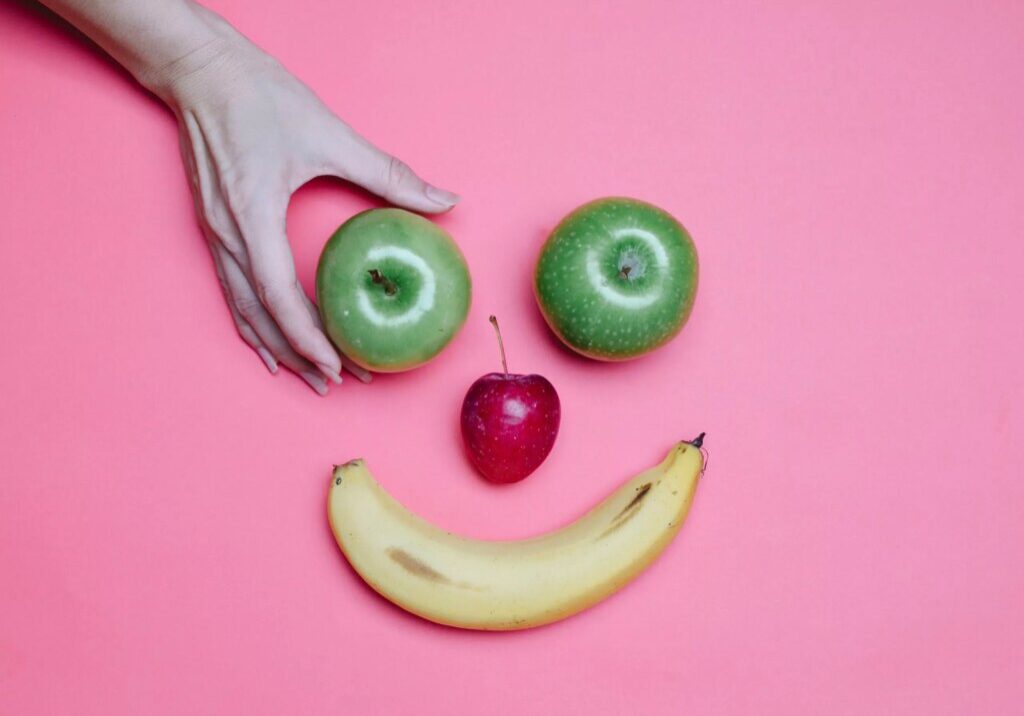 2 apples, a cherry, and a banana in the shape of a smiley face