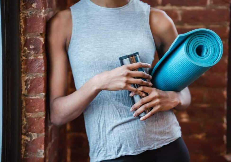 Woman holding a reusable water bottle and yoga mat