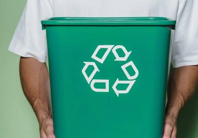 A man holding a green recycling bin