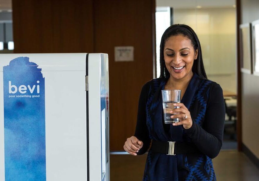 Smiling woman holding a glass of water next to a Bevi standup machine